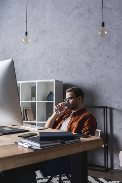 Jungunternehmer trinkt Wasser und schaut auf den Computer — Stockfoto