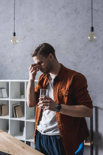 Junger Mann mit Kopfschmerzen hält Glas Wasser in der Hand — Stockfoto