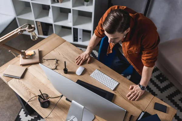 Hochwinkelaufnahme eines jungen Geschäftsmannes, der im Büro auf Computerbildschirm blickt — Stockfoto