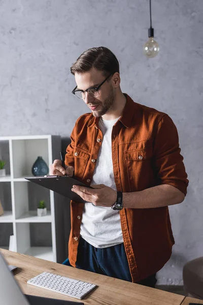 Stylischer Jungunternehmer mit Klemmbrett im modernen Büro — Stockfoto