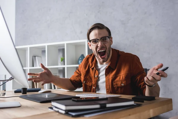 Angry designer sitting at workplace and screaming at camera — Stock Photo
