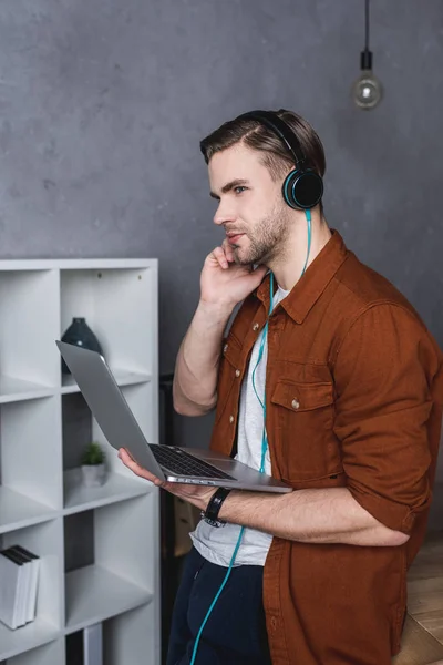 Jeune homme avec ordinateur portable écoutant de la musique avec écouteurs — Photo de stock