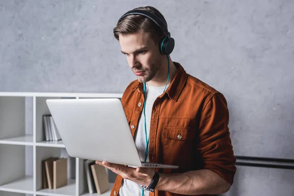 Joven hombre guapo en los auriculares que trabajan con el ordenador portátil - foto de stock