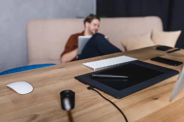 Designerin sitzt im Büro auf der Couch mit Tablet und Computer im Vordergrund — Stockfoto