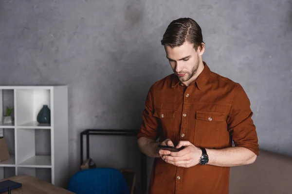 Schöner junger Mann mit Smartphone im Büro — Stockfoto