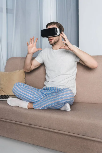 Joven en pijama y casco de realidad virtual en casa - foto de stock
