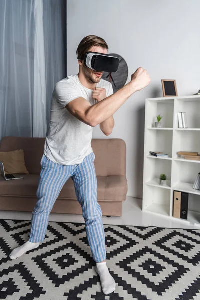 Young man in virtual reality headset and pajamas playing fighting game — Stock Photo