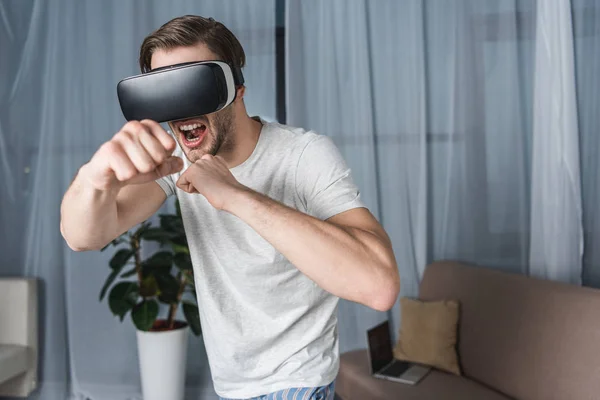 Hombre joven enojado en auriculares de realidad virtual juego de lucha - foto de stock