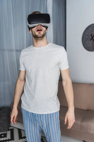 Shocked young man in pajamas and virtual reality headset — Stock Photo