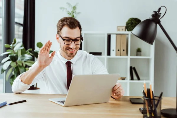 Bonito sorridente empresário acenando e fazendo chamada de vídeo no laptop — Fotografia de Stock