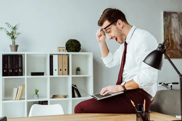 Hombre de negocios excitado utilizando el ordenador portátil en la oficina moderna - foto de stock