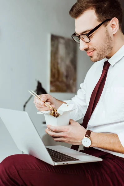 Hombre de negocios con estilo con portátil comer fideos en la oficina - foto de stock