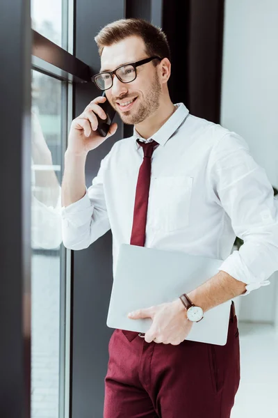 Uomo d'affari che parla su smartphone e tiene il computer portatile in ufficio moderno — Foto stock