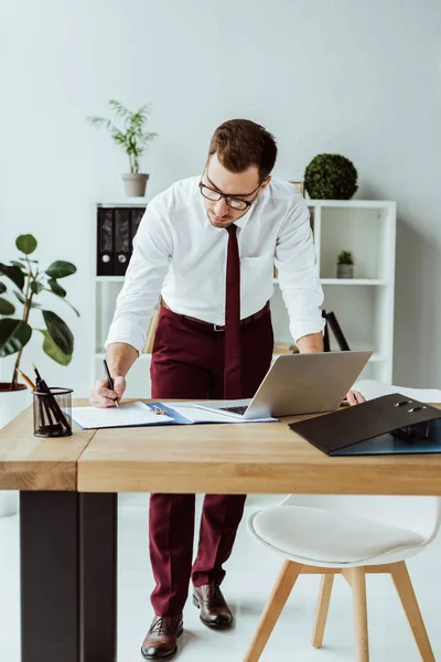 Bell'uomo d'affari che fa scartoffie sul posto di lavoro con il portatile — Foto stock