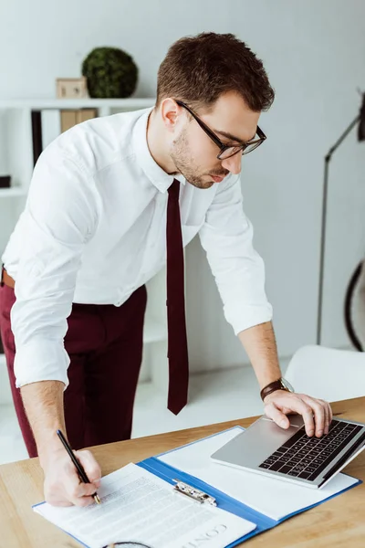 Handsome businessman doing paperwork and working with laptop in office — Stock Photo