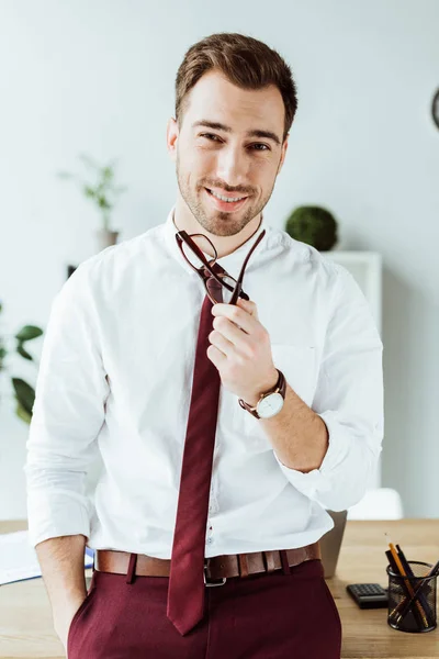 Apuesto hombre de negocios sonriente con gafas posando en la oficina moderna - foto de stock