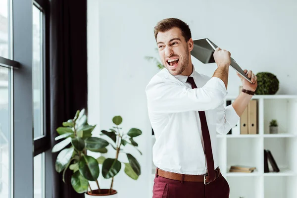 Homme d'affaires agressif criant et jetant ordinateur portable dans le bureau moderne — Photo de stock