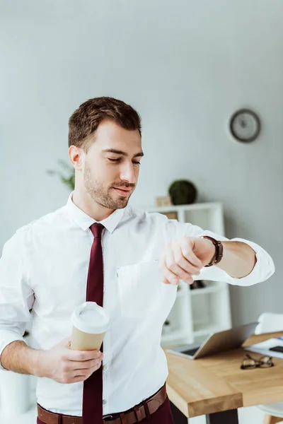 Бизнесмен с одноразовой чашкой кофе смотрит на наручные часы — стоковое фото