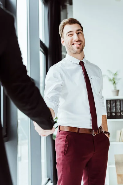 Homem de negócios piscando e apertando as mãos com colega no escritório — Fotografia de Stock