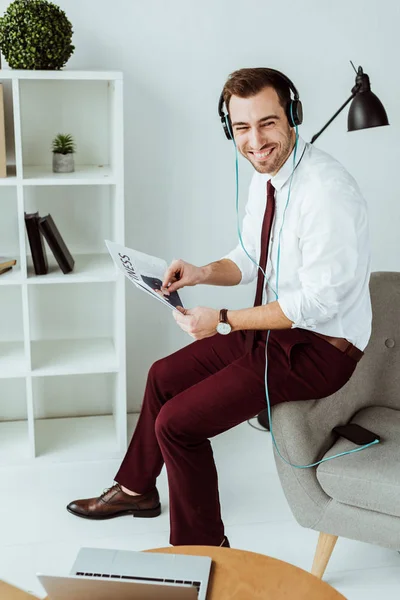 Alegre empresario escuchando música en los auriculares y leyendo el periódico - foto de stock