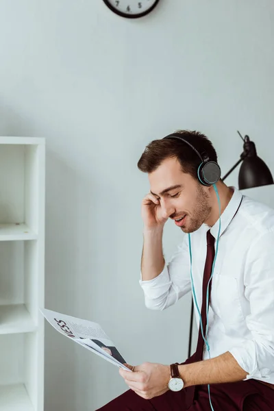 Giovane uomo d'affari che ascolta musica in cuffia e legge giornali — Foto stock