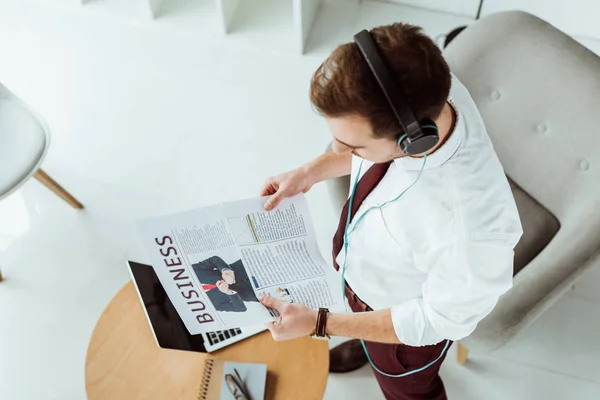 Handsome businessman in headphones reading newspaper — Stock Photo