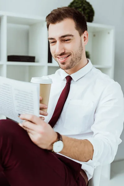 Elegante hombre de negocios sonriente con café para ir a leer el periódico en la oficina - foto de stock