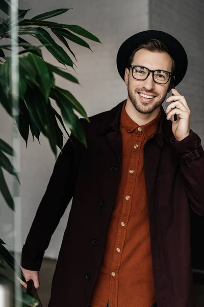 Handsome fashionable man in eyeglasses and hat talking on smartphone — Stock Photo