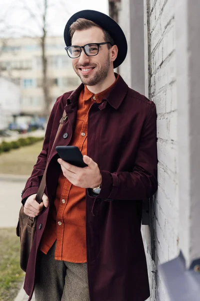 Hombre de moda guapo con bolsa usando teléfono inteligente - foto de stock