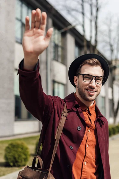 Joven guapo con bolsa saludando a alguien — Stock Photo
