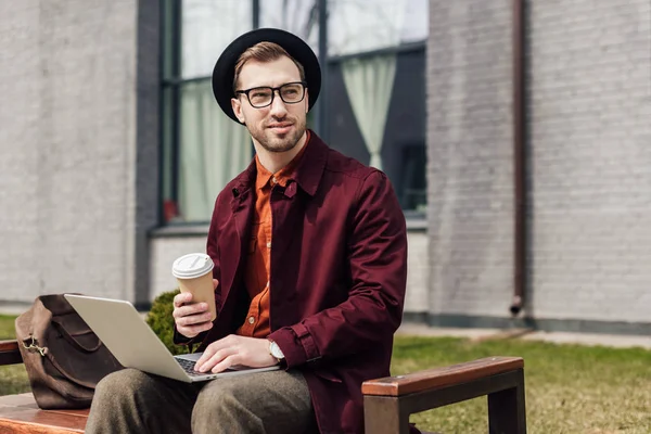 Homem elegante bonito com café para ir usando laptop — Fotografia de Stock