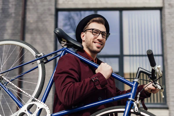 Guapo hombre de moda llevando bicicleta en el hombro - foto de stock