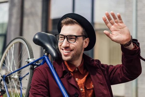 Guapo hombre de moda saludando y llevando bicicleta - foto de stock