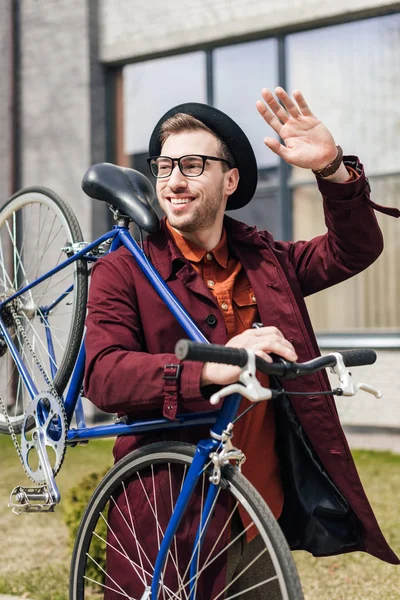 Bonito sorrindo homem acenando e carregando bicicleta — Fotografia de Stock