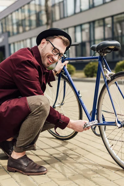 Schöner lächelnder Mann repariert Fahrrad auf der Straße — Stockfoto