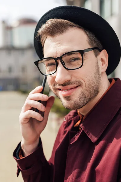 Bell'uomo sorridente in occhiali e cappello che parla su smartphone — Foto stock