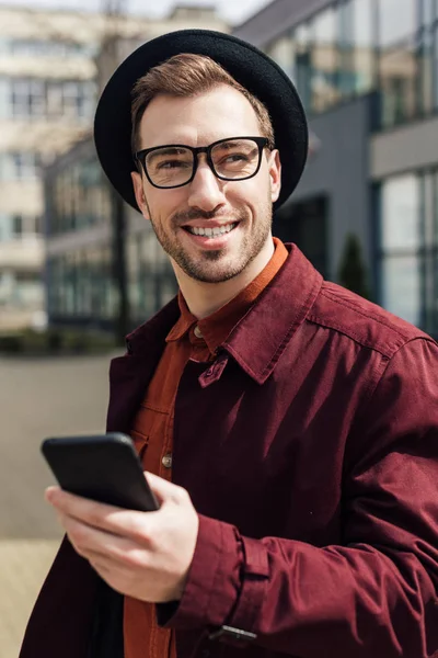 Hombre guapo en gafas de moda usando teléfono inteligente - foto de stock