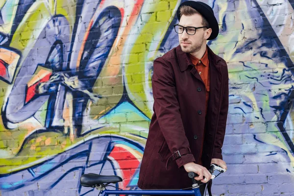 Homme élégant debout avec vélo au mur avec graffiti — Photo de stock