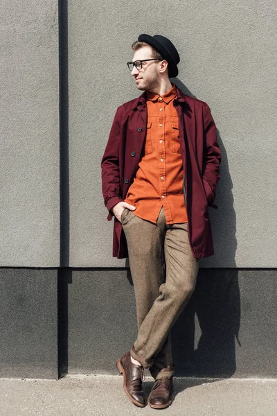 Handsome stylish man in trendy hat standing at grey wall — Stock Photo