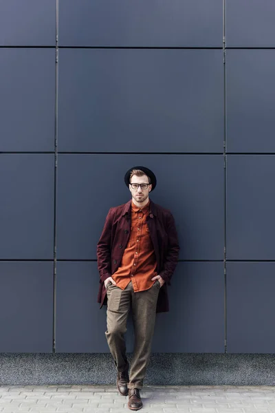 Bello uomo elegante in cappello in piedi al muro nero — Foto stock