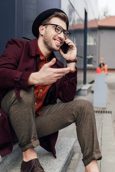 Улыбающийся мужчина в очках и шляпе разговаривает на смартфоне — стоковое фото