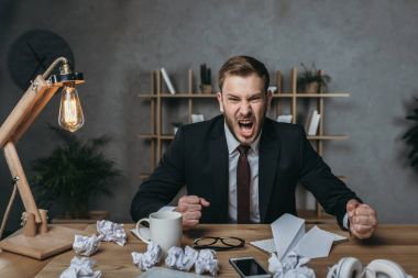 angry businessman yelling while sitting at workplace clipart