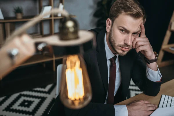 Uomo d'affari guardando lampada mentre seduto sul posto di lavoro — Foto Stock