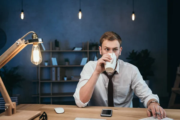 Businessman drinking coffee while working at office — Stock Photo, Image