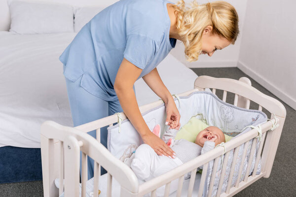 mother looking at baby in crib