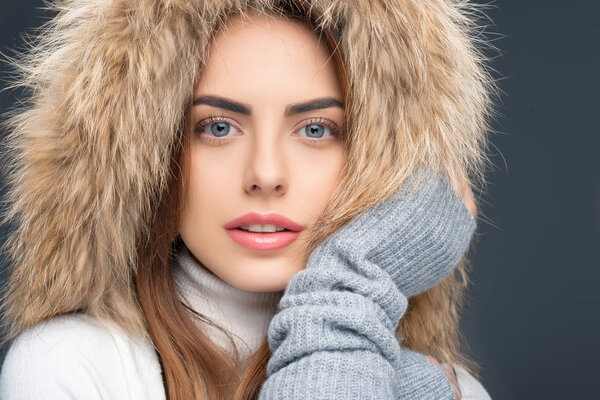 portrait of beautiful woman in fur hat and winter outfit, isolated on grey