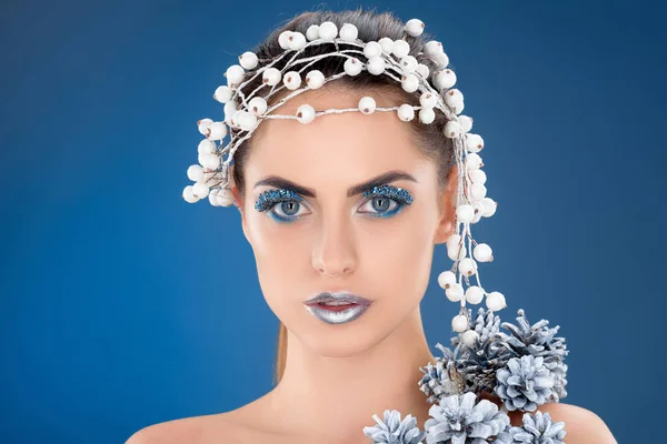 beautiful model with hair accessory, christmas pine cones, winter makeup and glitter, isolated on blue