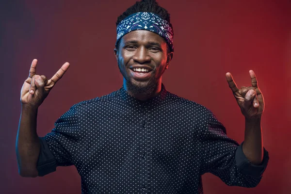 Happy african american man showing rock signs isolated on burgundy — Stock Photo, Image