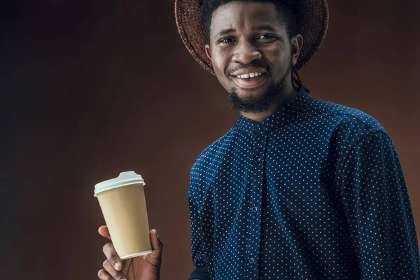 Smiling african american man with disposable coffee cup isolated on brown — Stock Photo, Image