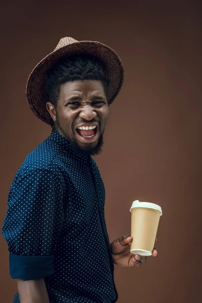 Afryki amerykański mężczyzna krzyczy z kubkiem kawy jednorazowe na brązowym tle — Darmowe zdjęcie stockowe